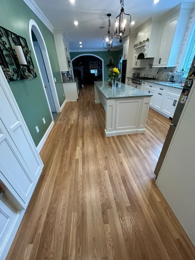 New oak hardwood running from the hallway into a white kitchen with an island